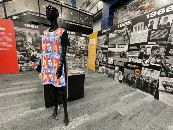 a museum exhibit featuring a mannequin with political clothing and a timeline display of the 1960s