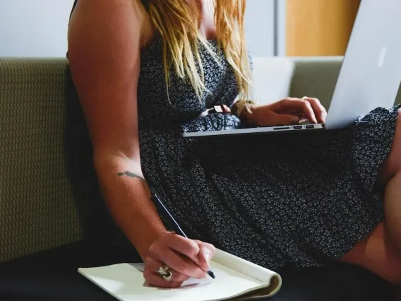 a woman writing with a notebook and a laptop