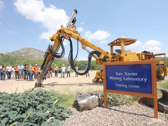 a group gathered near the san xavier mining laboratory with a large mining machine nearby