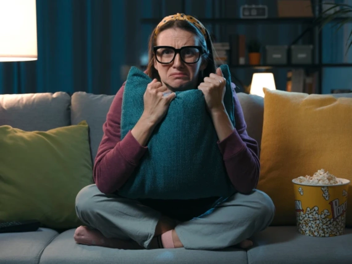 woman clutching a pillow on a couch next to a bucket of popcorn