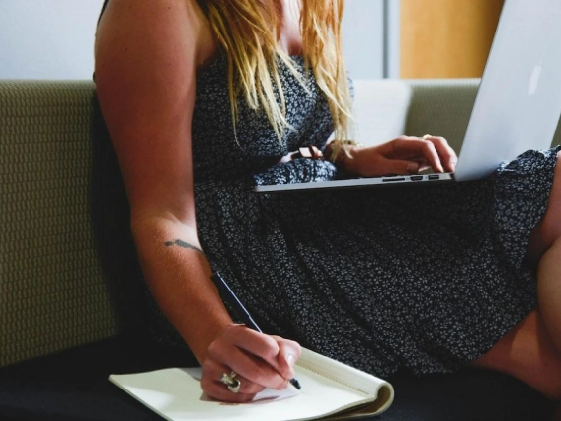 a woman writing with a notebook and a laptop