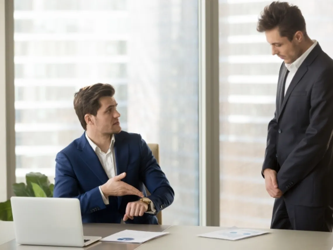 a standing man talking to a man sitting at a desk