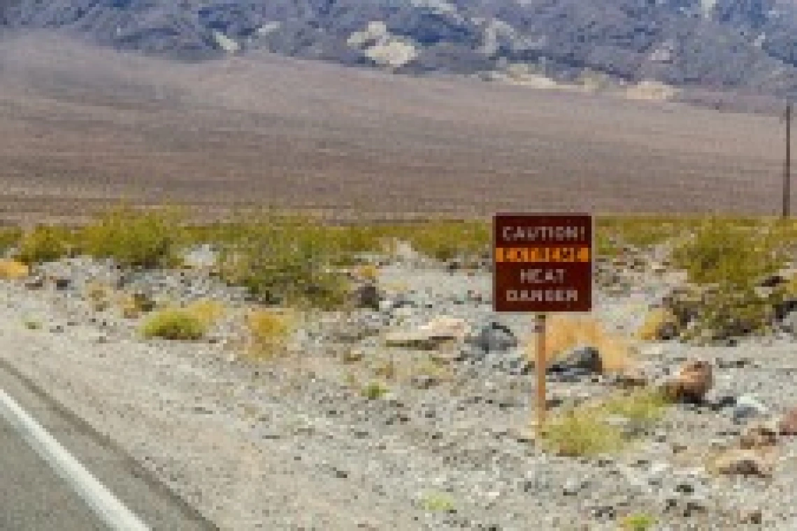 a sign that says "caution extreme heat danger" next to a road in a desert