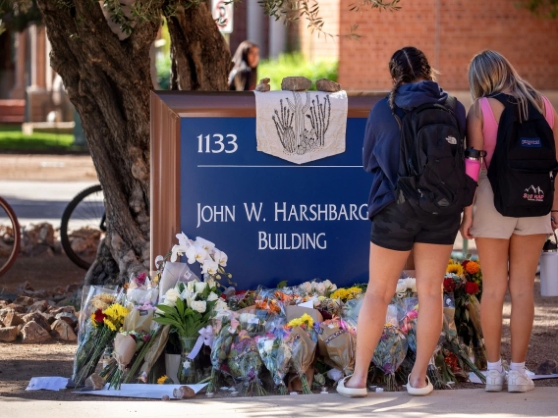 two students look at a building sign with flowers around it